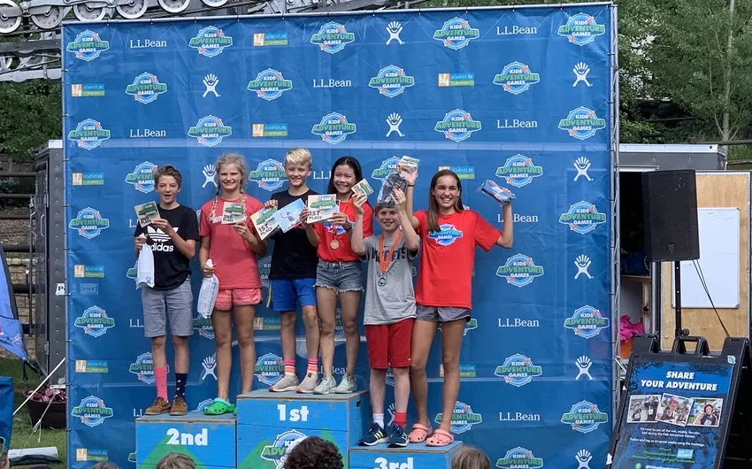 Kids on the podium at the Vail Kids Adventure Race in front of the event backdrop, holding prizes